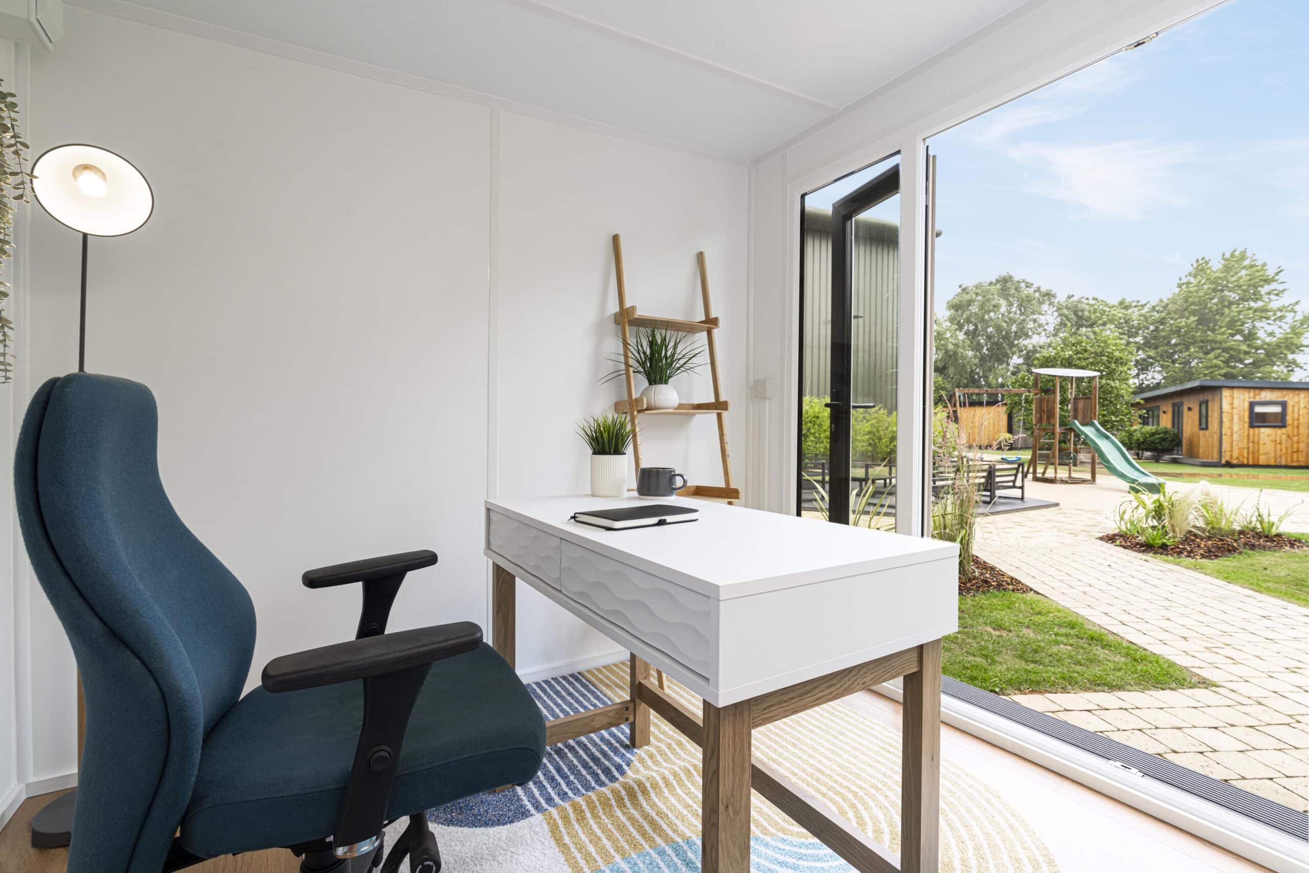 Interior of garden office showing white desk and office chair facing out into the garden